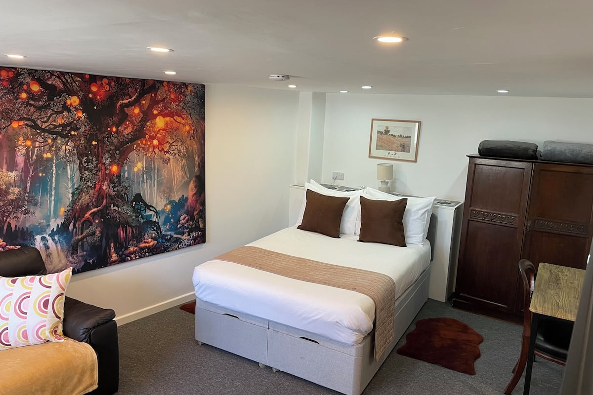 A bedroom with a bed, a nightstand, a dresser, a painting, and a chair.