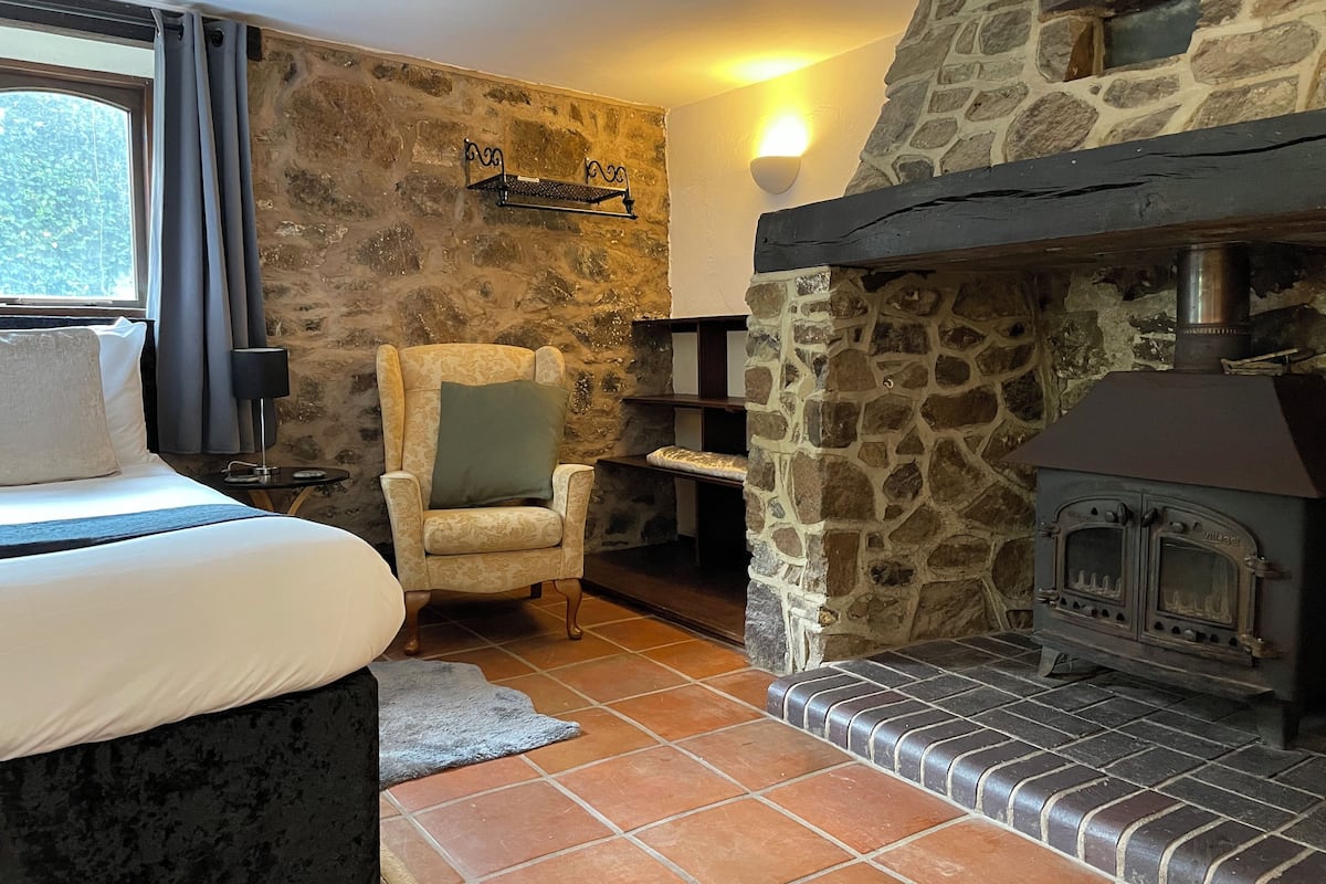 A cozy room with a stone wall, a fireplace, a bed with a pillow, and a chair.