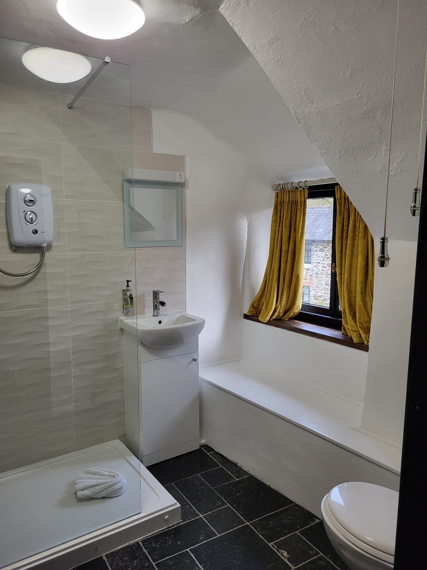 A bathroom with a glass-enclosed shower, a sink, a toilet, and a window with curtains.