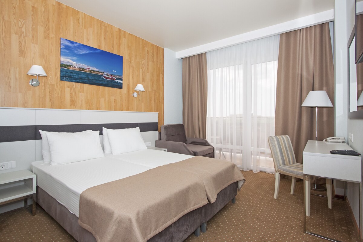 A hotel room with a large bed, a desk, a chair, and a window with curtains.