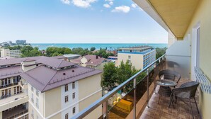 A balcony with wicker chairs and a table, overlooking a cityscape and a body of water. - SunMarInn Resort (Anapa)