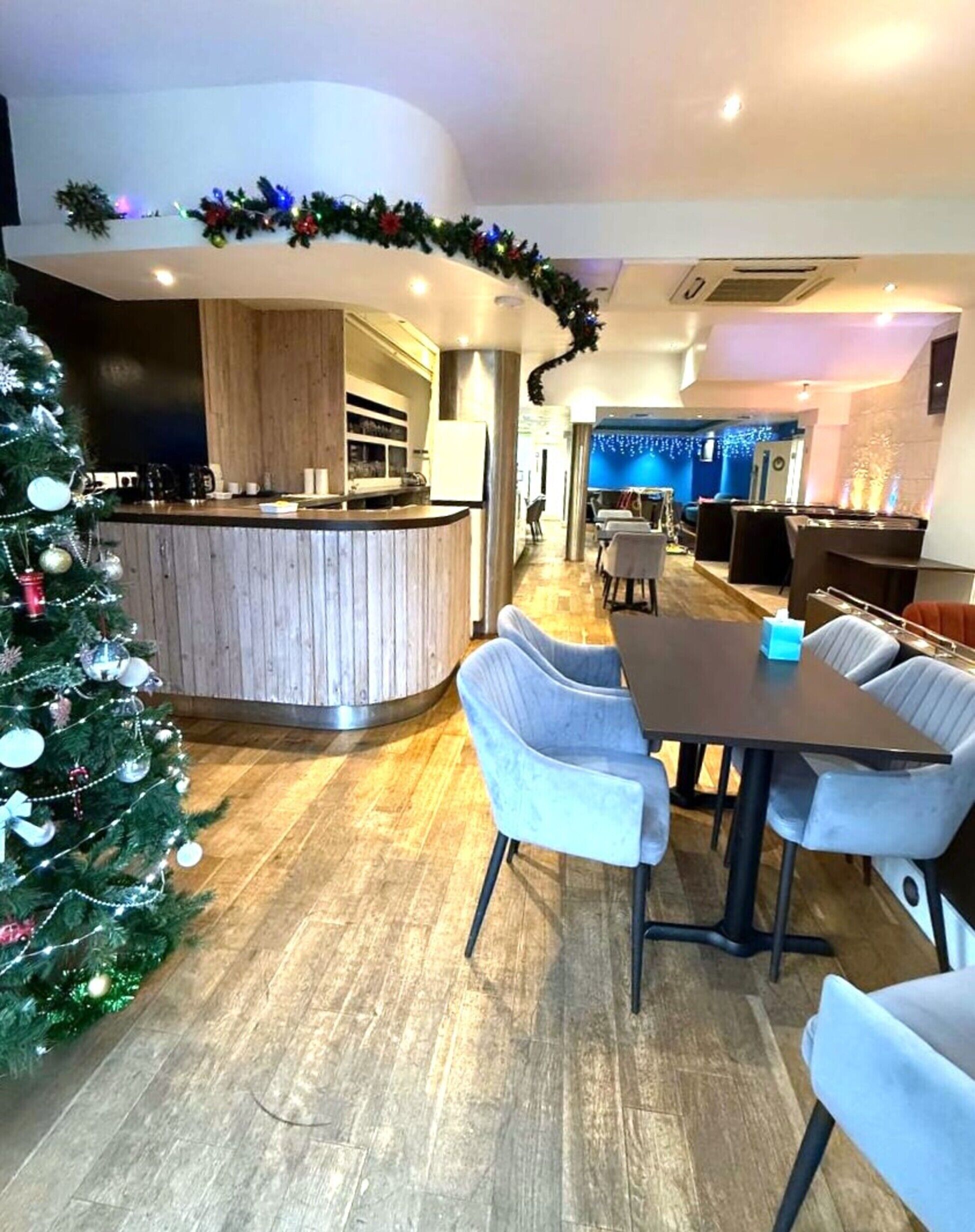 Um hall de hotel moderno com um balcão de recepção curvo, um pinheiro de Natal e uma área de refeições com cadeiras de cor clara.