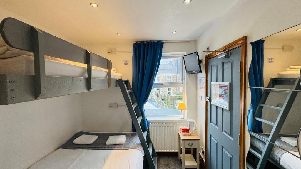 A compact hotel room with bunk beds, a small desk, a television, and a window with curtains.