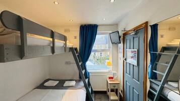 A compact hotel room with bunk beds, a small desk, a television, and a window with curtains.