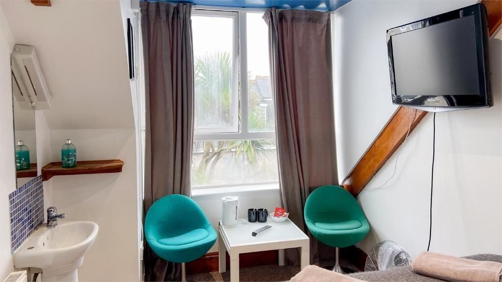 A small room with a window, a sink, a mirror, a television, and two chairs.