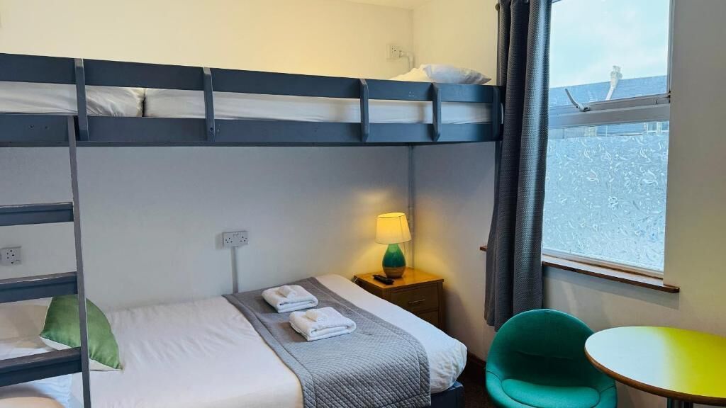 Habitación con literas, una cama individual, una mesita de noche con lámpara, una pequeña mesa y vistas al mar a través de una ventana.