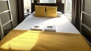 Hotellihuone, jossa on sänky, kaksi tyynyä, ikkuna ja näkymä ulkopuolella olevaan rakennukseen.