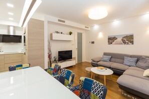 A modern living room with a sofa, a dining table, and a TV. - Antonio Luxury Beach Suites (Dubrovnik)