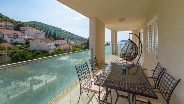 Un balcon avec une table et des chaises, donnant sur un quartier résidentiel et des collines.