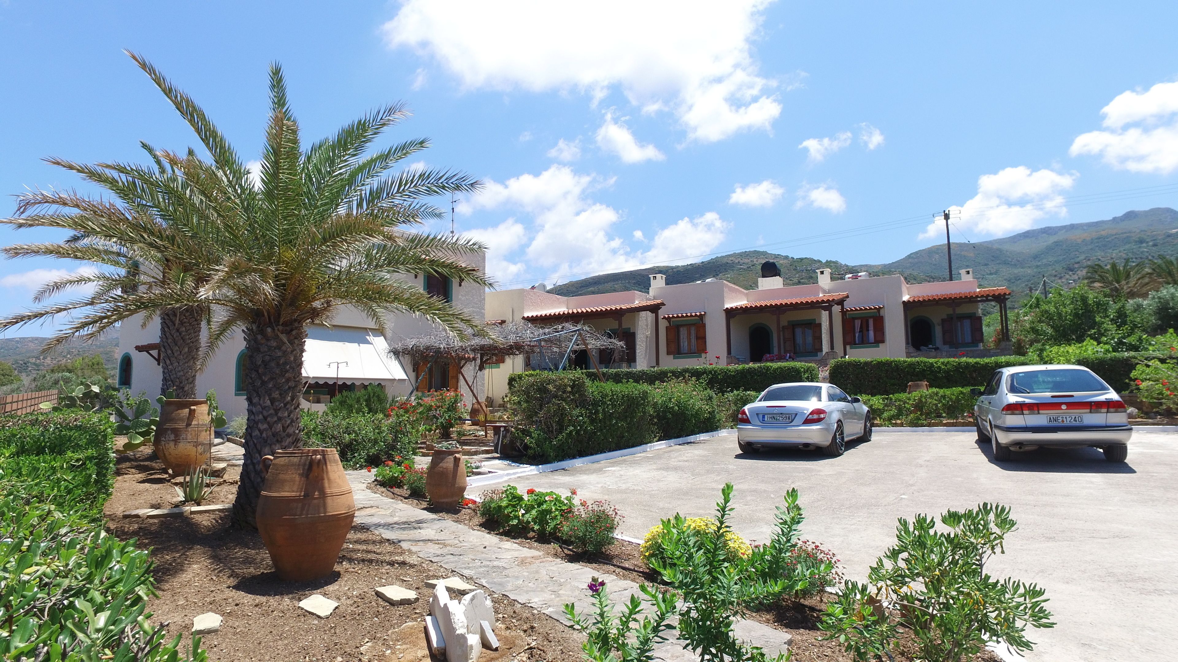 Una villa in stile mediterraneo con vialetto lastricato, una palma e montagne sullo sfondo.