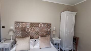 A neatly arranged bedroom with a patterned headboard, two bedside tables with lamps, a wardrobe, and a bed with two pillows.