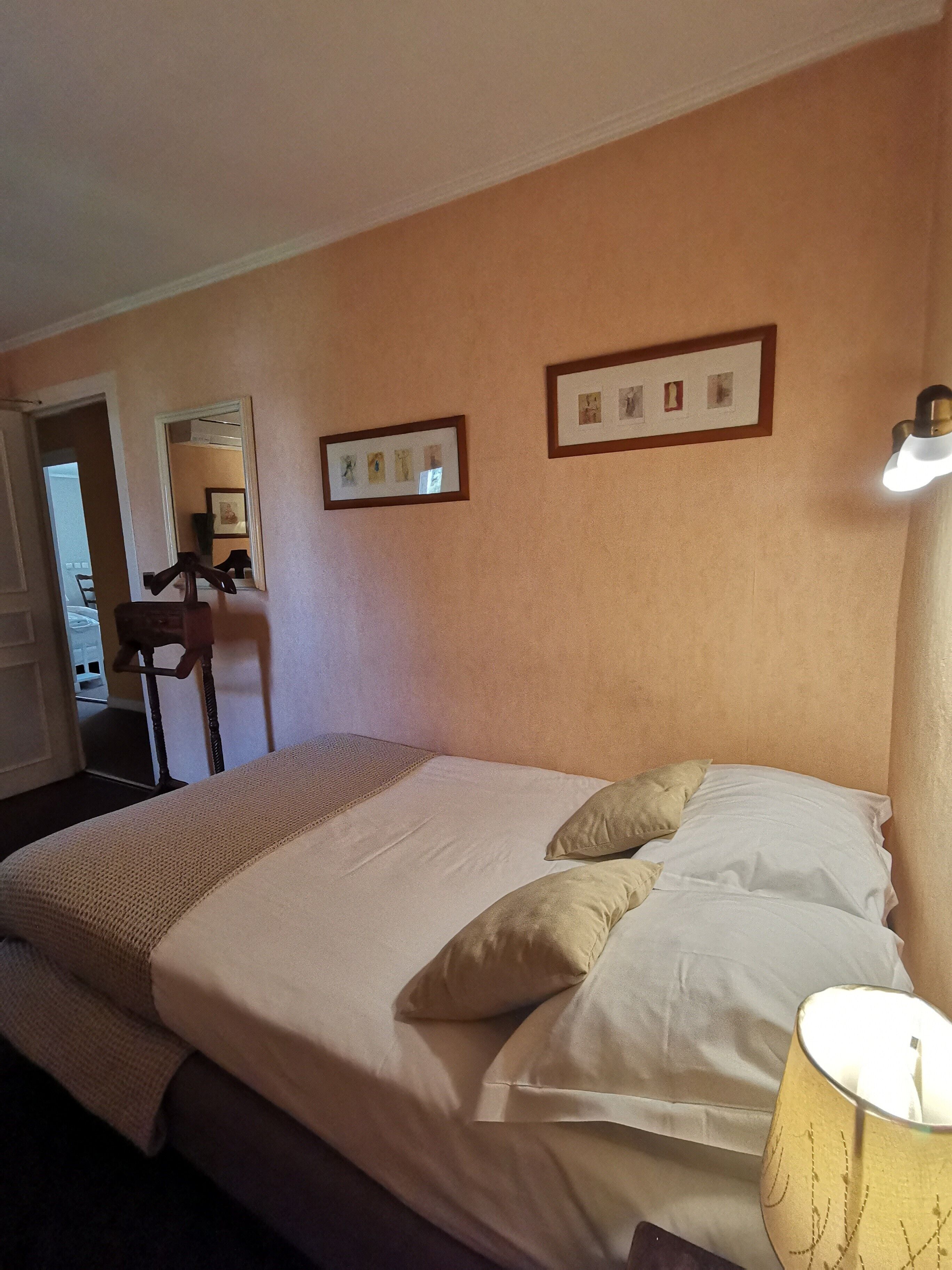 A hotel room with a large bed, a bedside lamp, and two framed pictures on the wall.