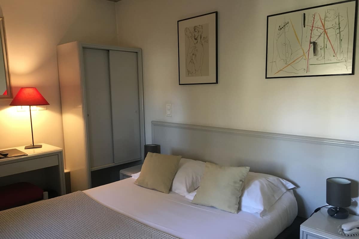 A neatly arranged hotel room with a bed, bedside table, lamp, and artwork on the wall.