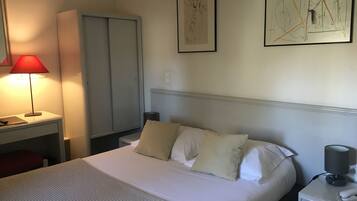 Una habitación de hotel ordenada con cama, mesita de noche, lámpara y una obra de arte en la pared.