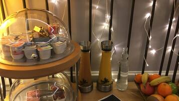 Un bufé de desayuno con recipientes de yogur, una cafetera, una botella de agua y una cesta de frutas.