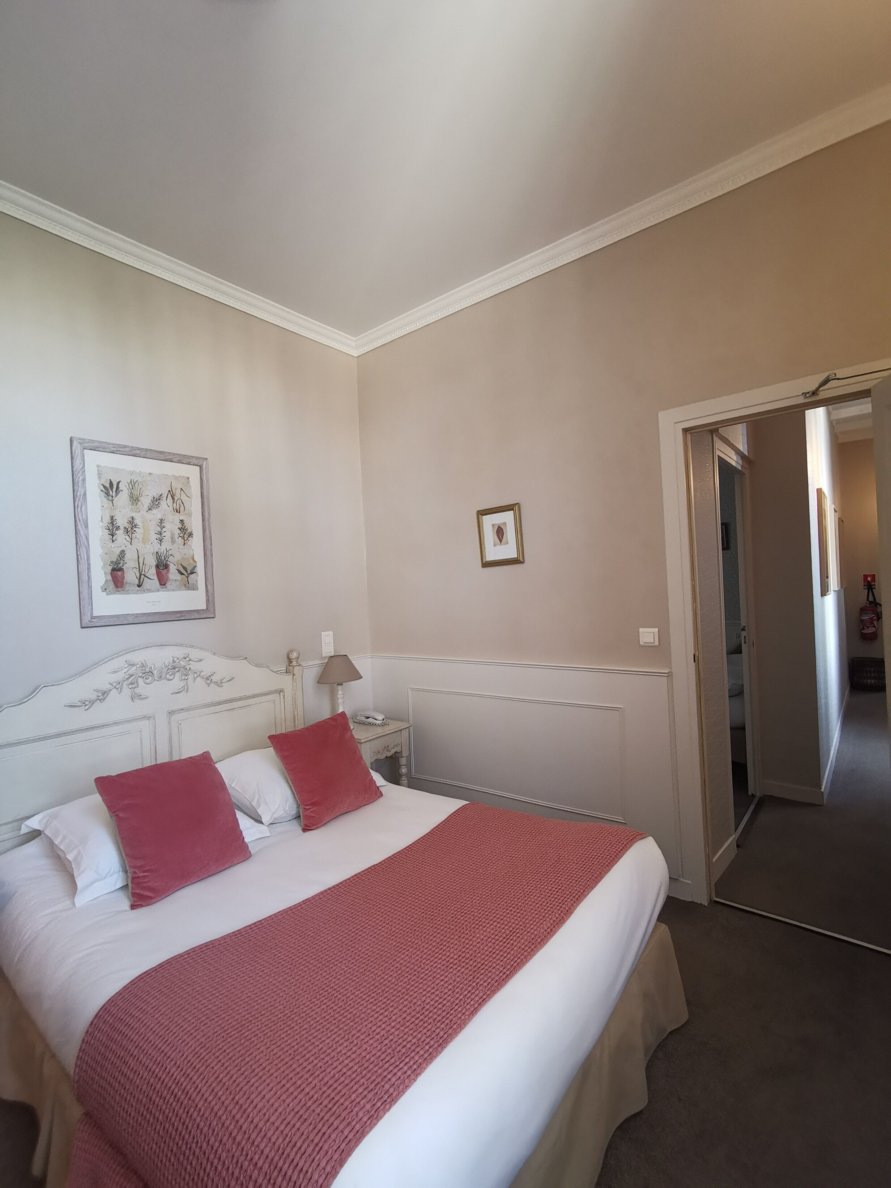 Una camera da letto con un letto, un comodino, una lampada, un'illustrazione botanica incorniciata e un termosifone.