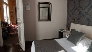 Habitación de hotel con cama, mesita de noche, espejo y vista al pasillo.
