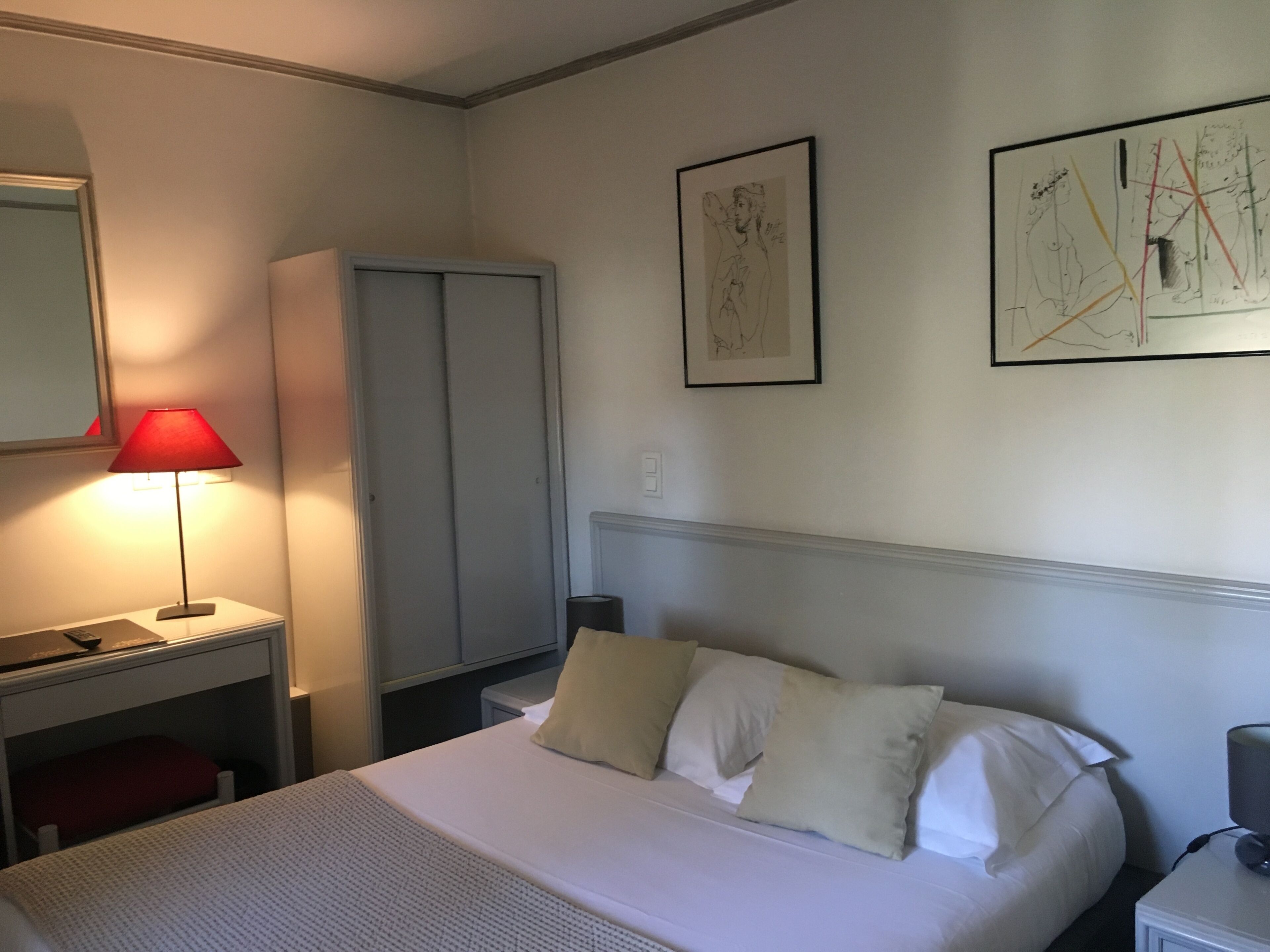 A hotel room with a bed, a desk, a chair, a wardrobe, and two wall art pieces.