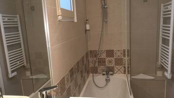 Baño con bañera, ducha y lavamanos. Hay una ventana sobre la ducha, y las paredes están cubiertas con un diseño estampado.