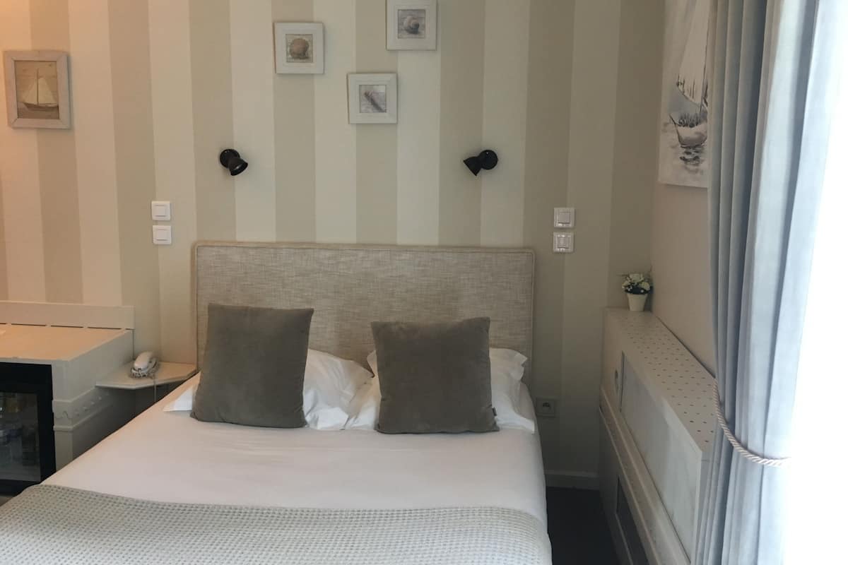 A hotel room with a bed, two wall-mounted lights, and three framed pictures on the wall.