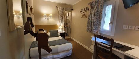 A hotel room with a bed, a desk, a chair, a TV, and a window with curtains.