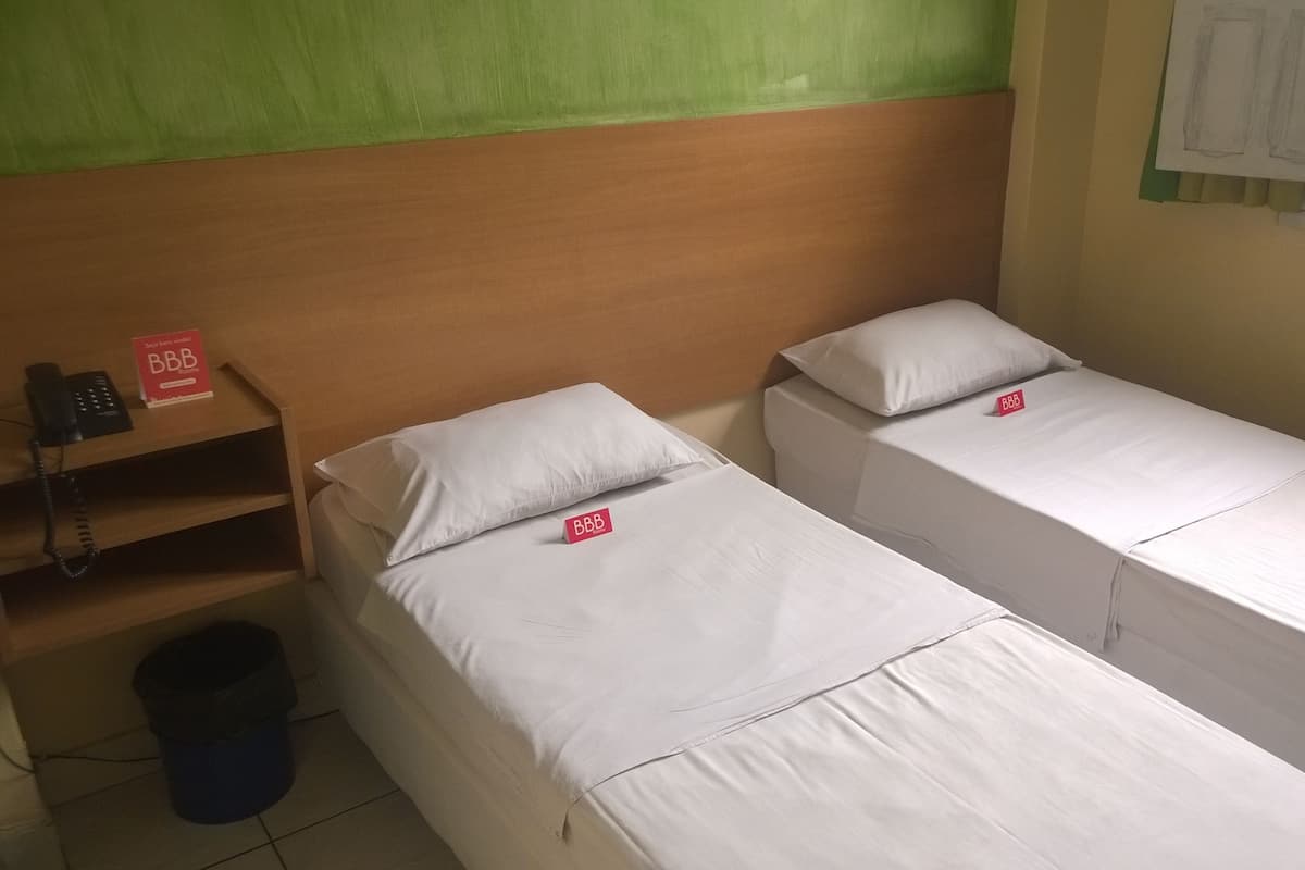 Une chambre avec deux lits simples, une tête de lit en bois, une petite étagère avec un téléphone et un panneau indiquant « Chambres BBB ».