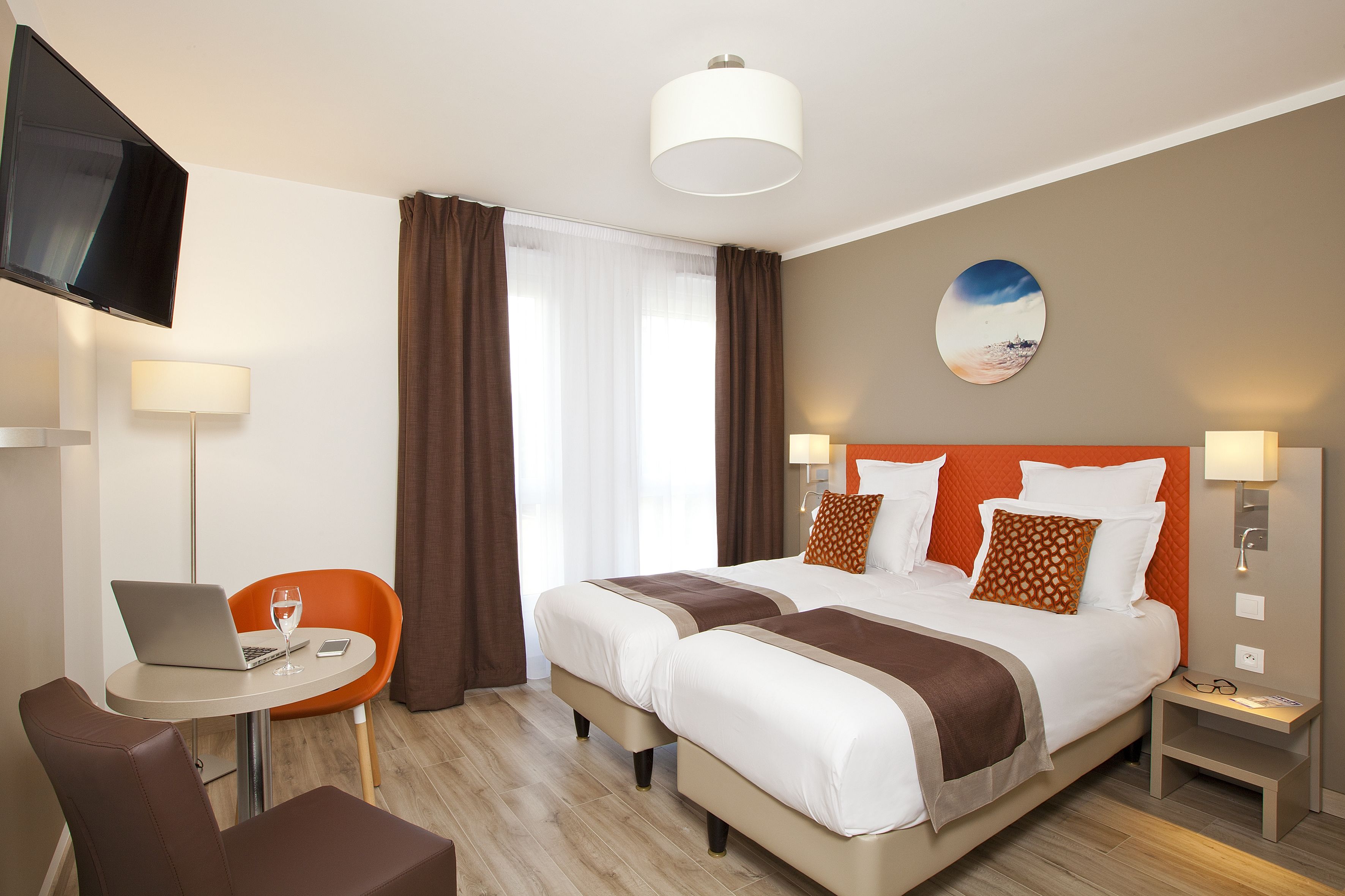 Une chambre d’hôtel équipée d’un lit, d’un bureau avec un ordinateur portable, d’une chaise et d’un téléviseur fixé au mur.