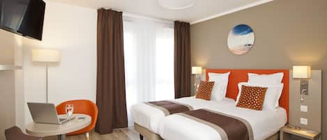 A hotel room with a bed, a desk with a laptop, a chair, and a TV mounted on the wall.