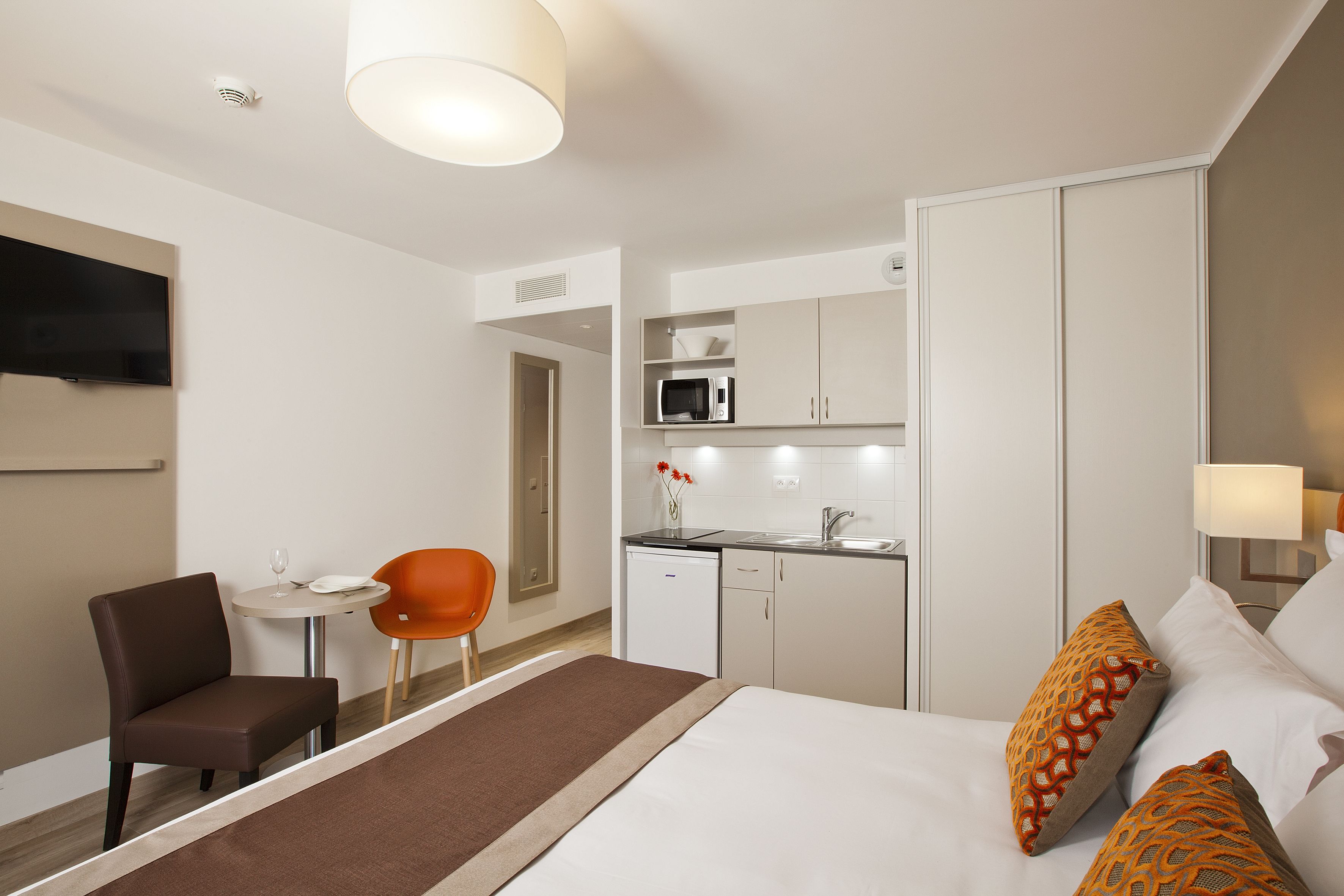 A hotel room with a bed, a desk, a chair, a microwave, and a television.