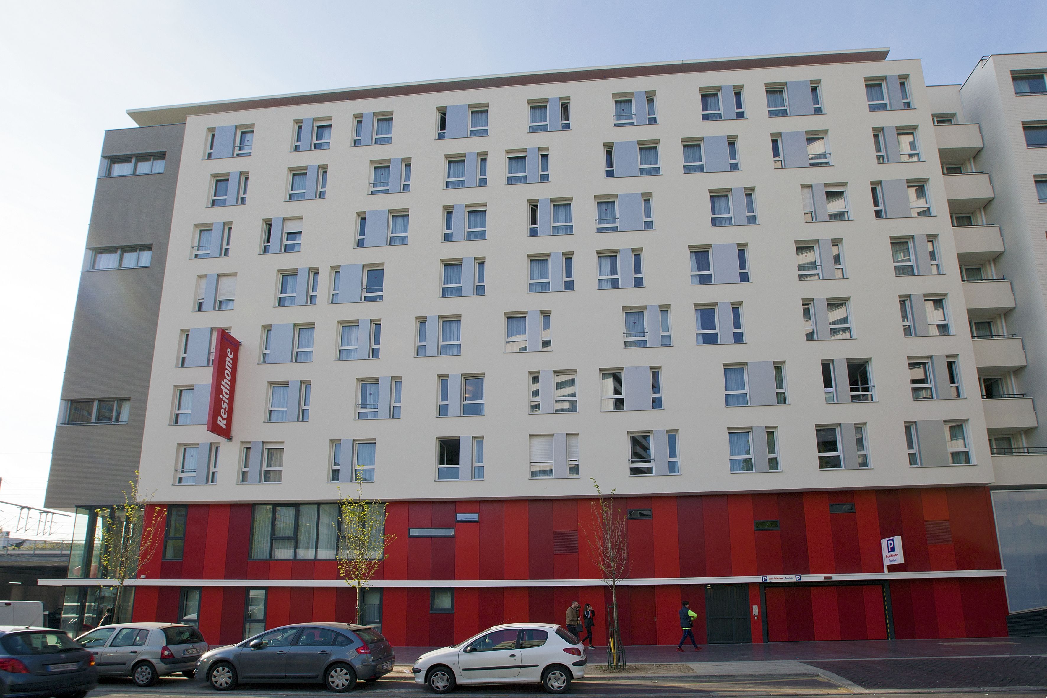 Un hotel de varios pisos con fachada roja y blanca, múltiples ventanas y un letrero de estacionamiento visible.