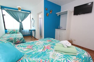 Un dormitorio con cama, televisor, espejo y baño visible a través de una puerta abierta.