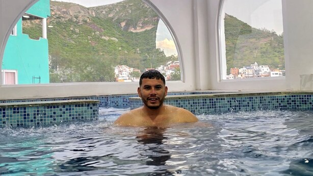 Um homem em uma piscina com janelas em arco e vista para uma paisagem montanhosa.