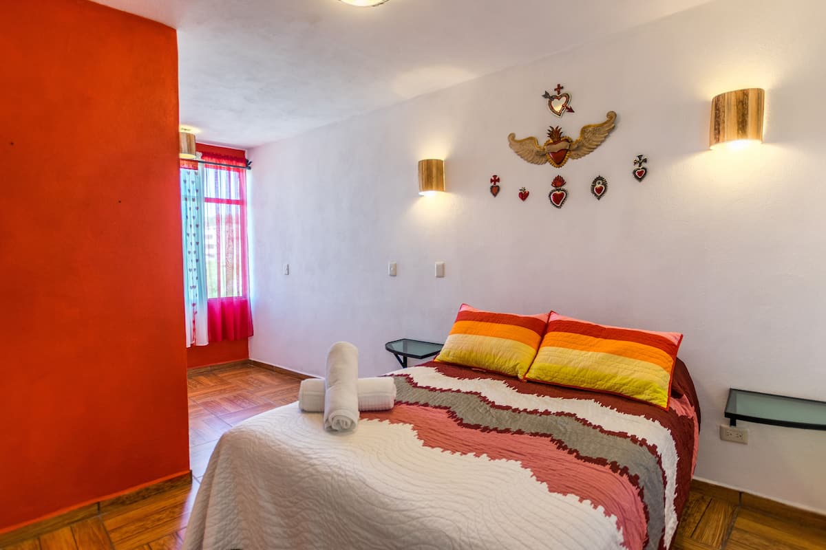A bedroom with a bed, pillows, a wall-mounted light, and a window with curtains.