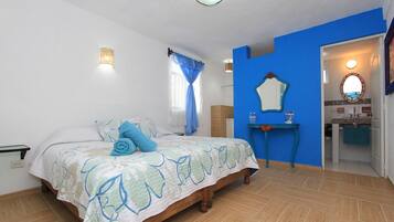 Un dormitorio con cama, mesita de noche, espejo y baño visible a través de una puerta abierta.