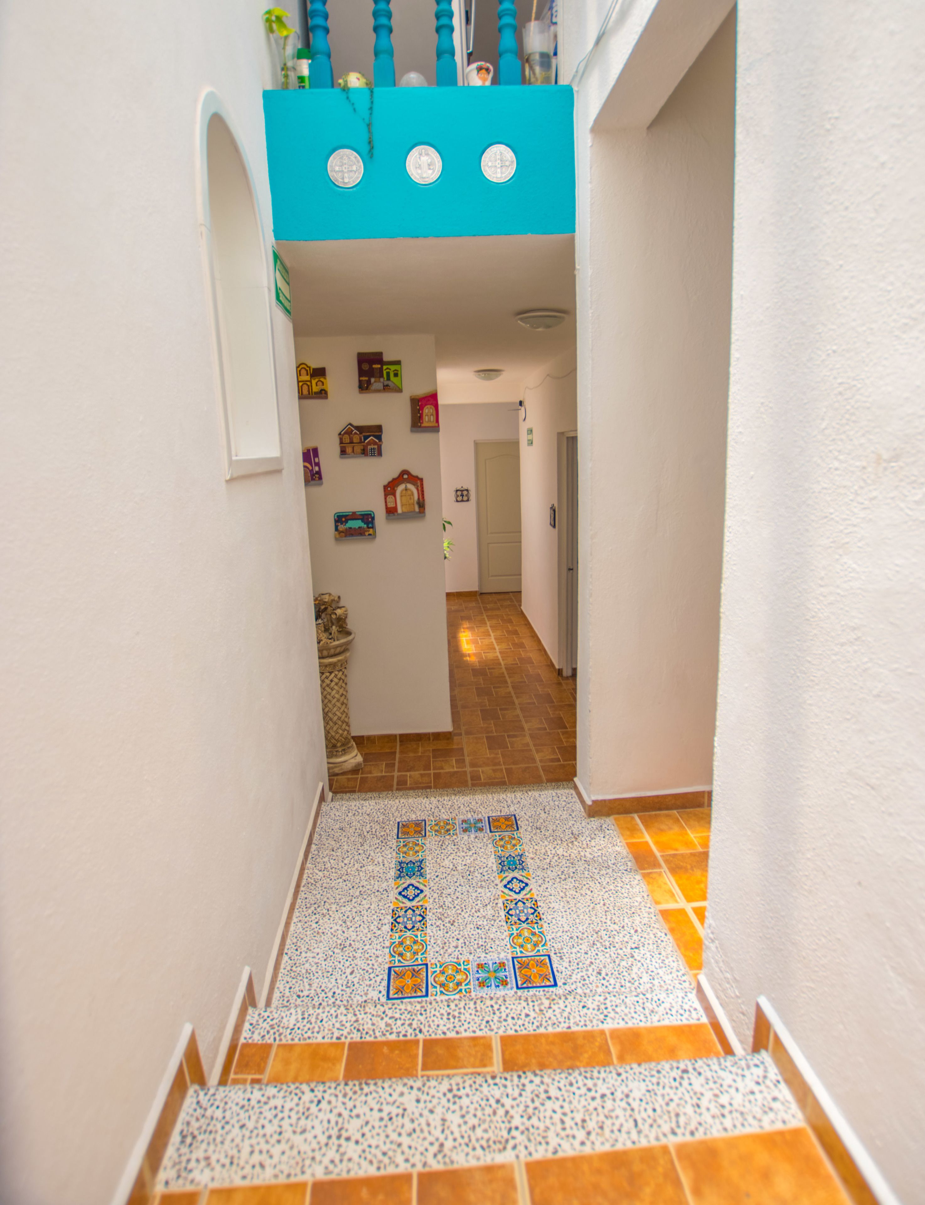 A narrow hallway with a tiled floor, a blue railing, and a door at the end.