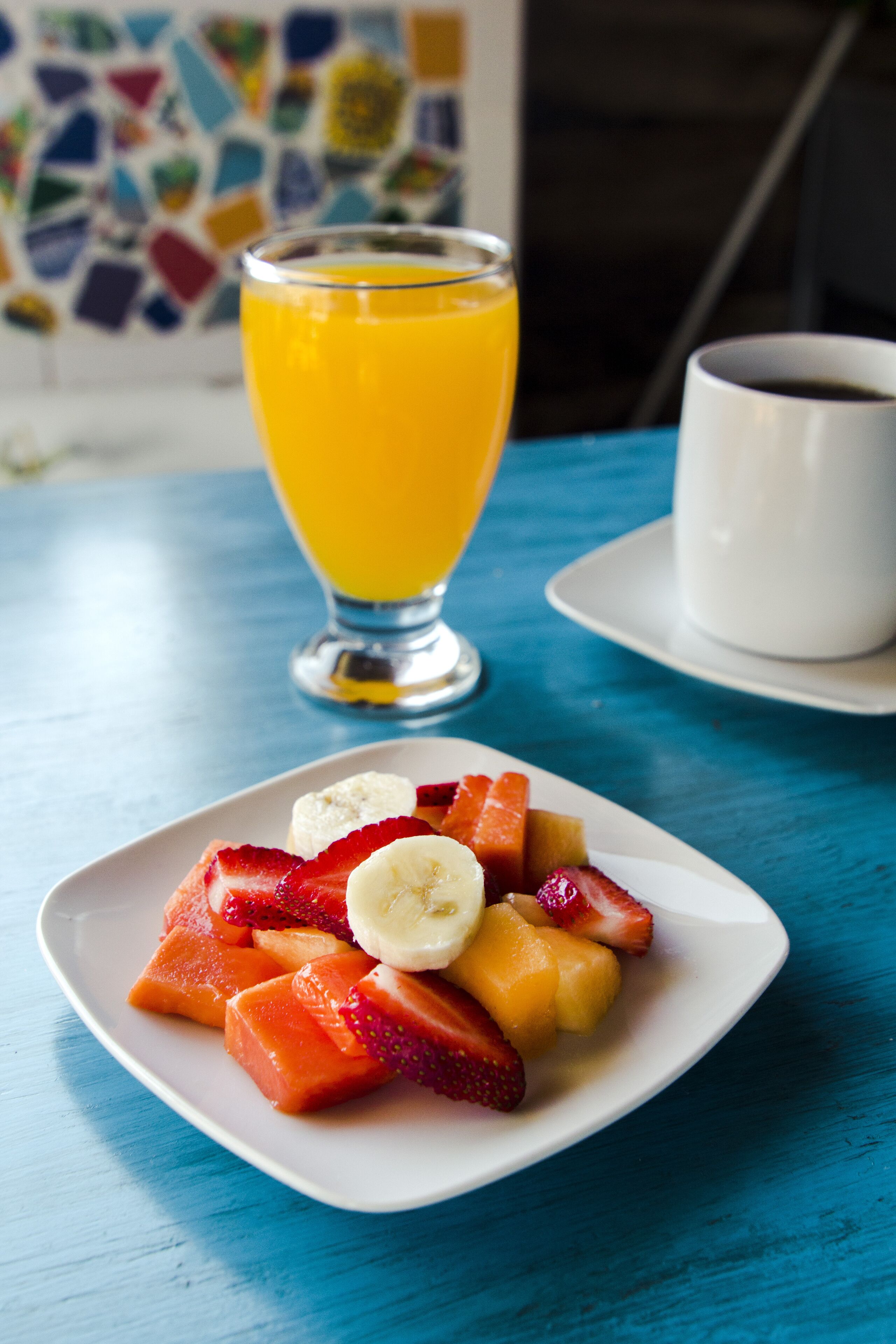 A plate of sliced fruits and a glass of orange juice on a blue table.