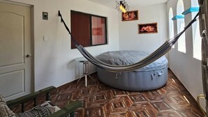 Quarto com rede, um pufe, uma mesa pequena e piso estampado.