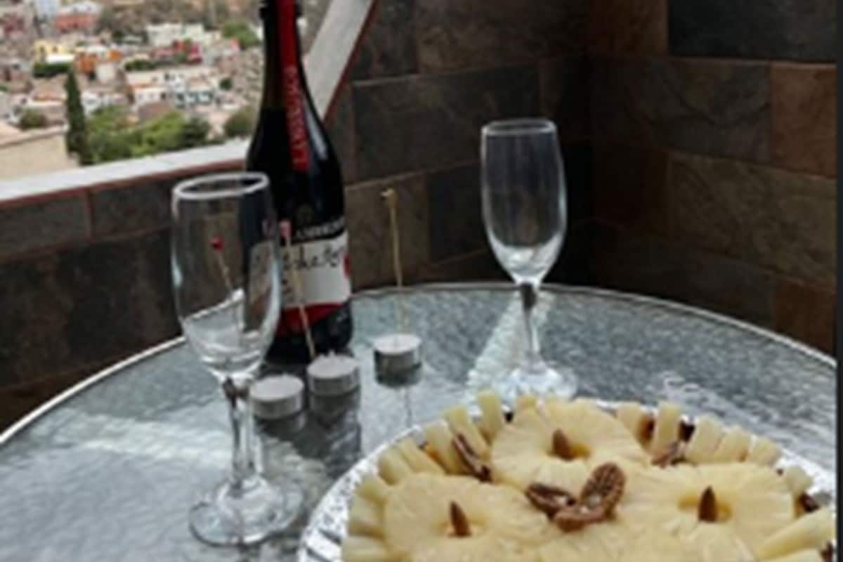 A table with a bottle of wine, two glasses, and a pie on a balcony overlooking a cityscape.