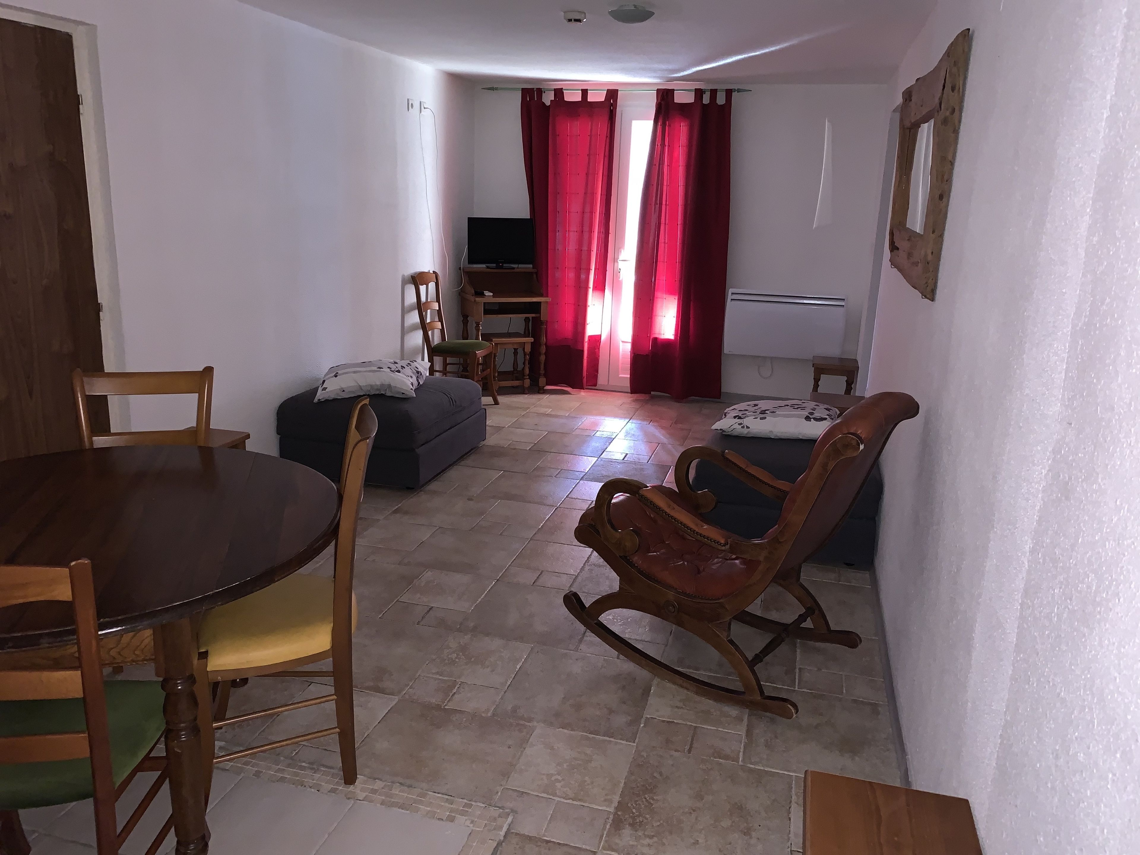 Uma sala de estar com um sofá, uma mesa de jantar com cadeiras, uma televisão e uma cortina vermelha.