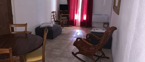 Uma sala de estar com um sofá, uma mesa de jantar com cadeiras, uma televisão e uma cortina vermelha.