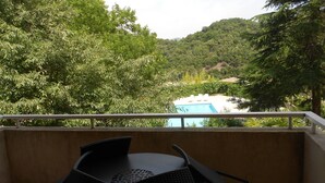 Un balcón con mesa y sillas que da a una piscina y abundante follaje.