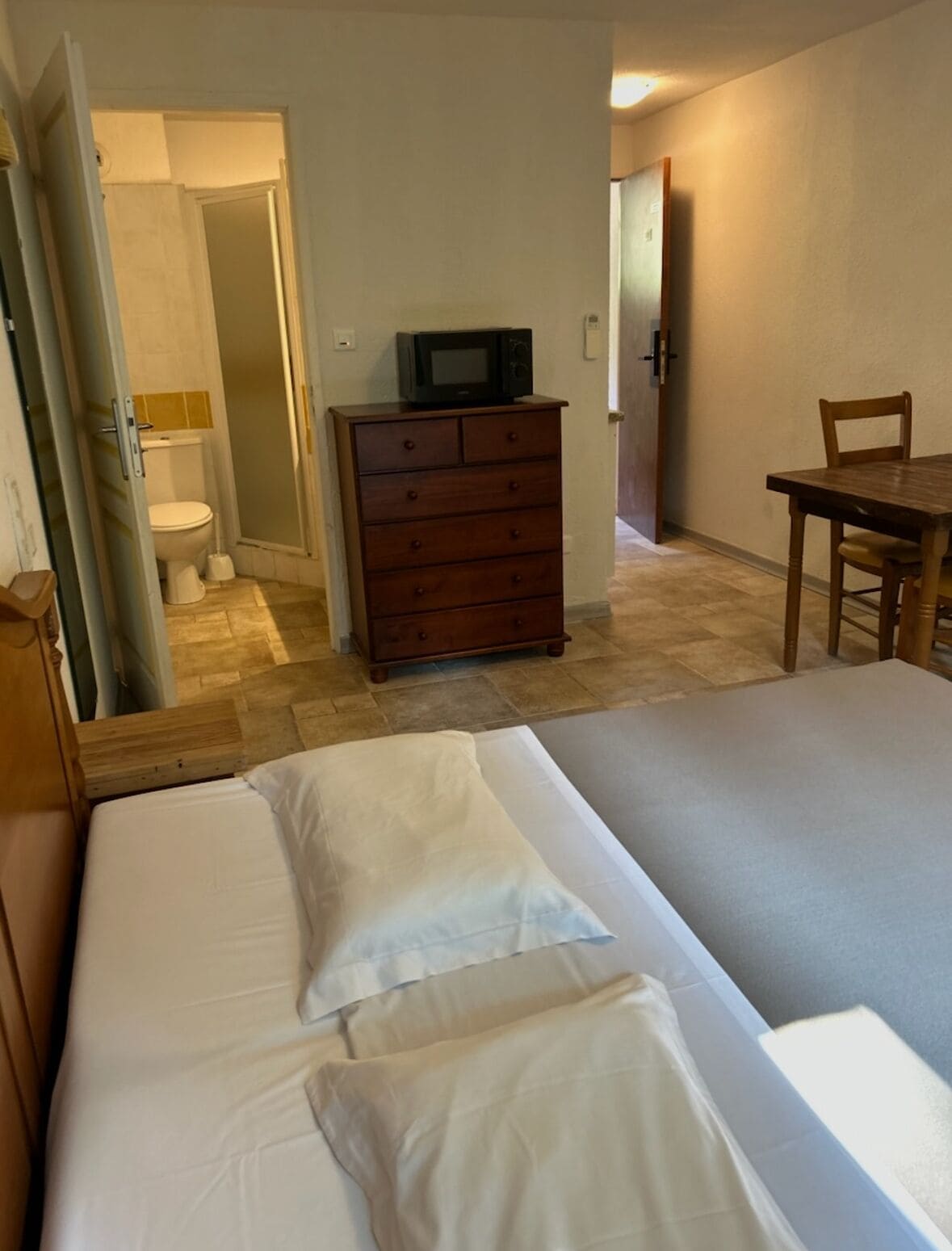 A bedroom with a bed, a dresser, a television, and a bathroom visible through an open door.
