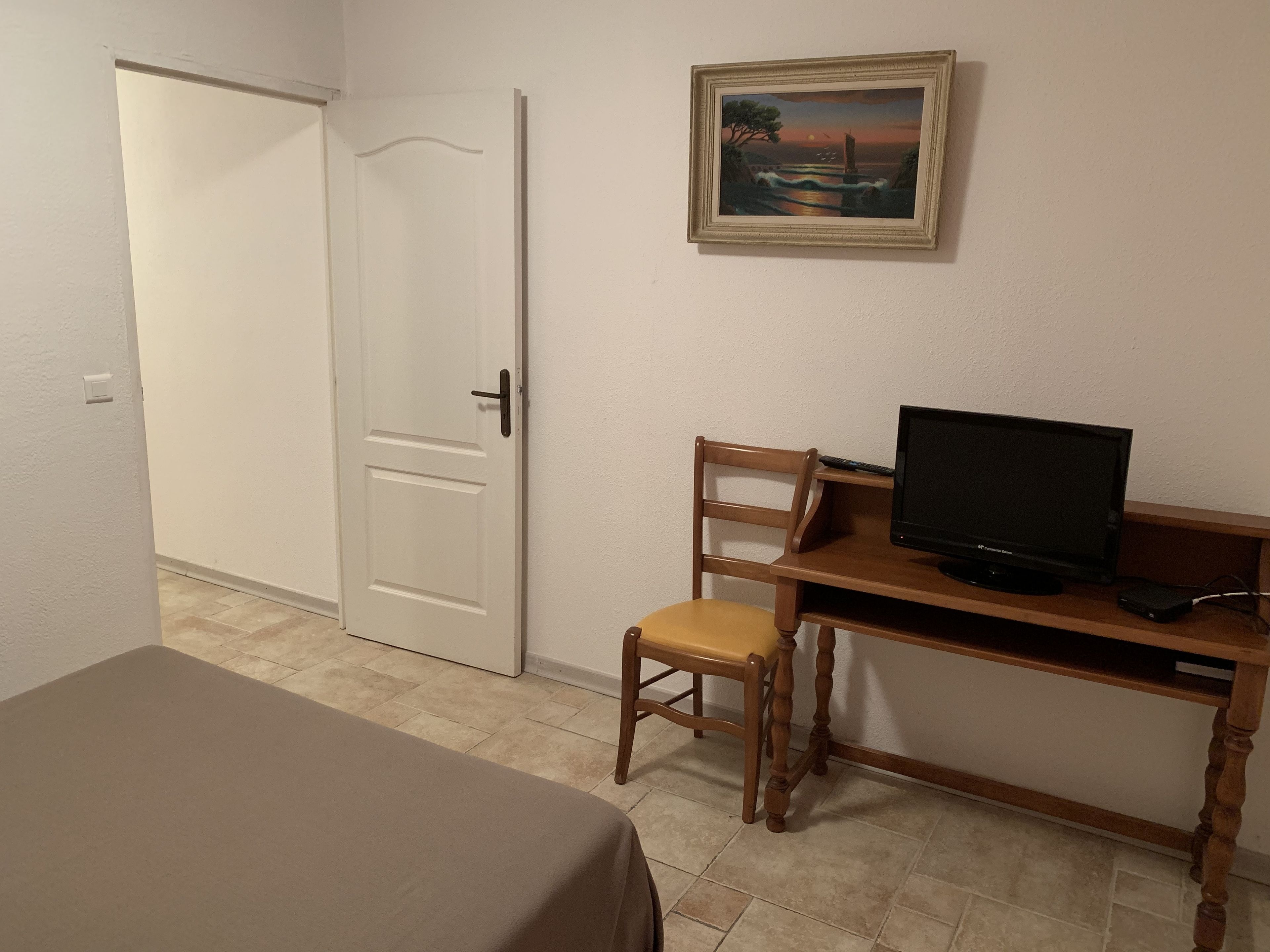 A room with a bed, a desk with a computer, a chair, and a door.
