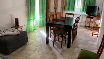 A living room with a sofa, a dining table with chairs, a television, and a cabinet.