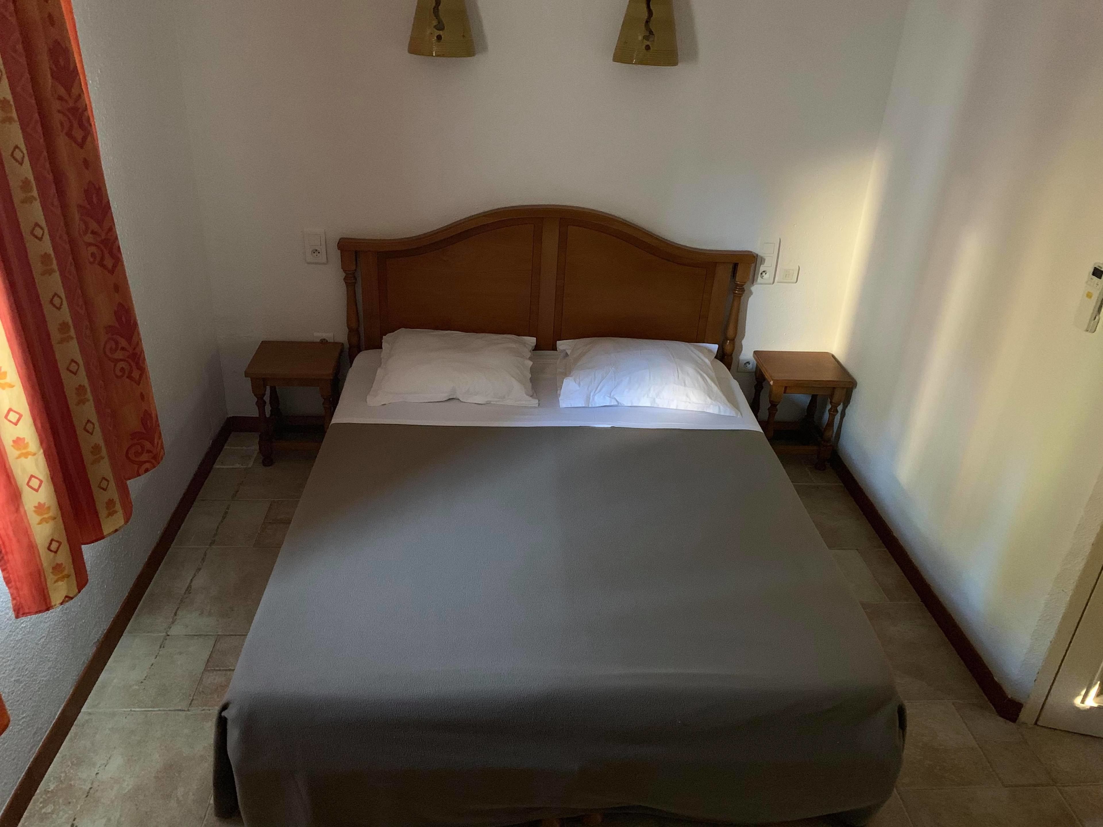 Een enkel bed met een houten hoofdbord, twee nachtkastjes en een gordijn aan de linkerkant.