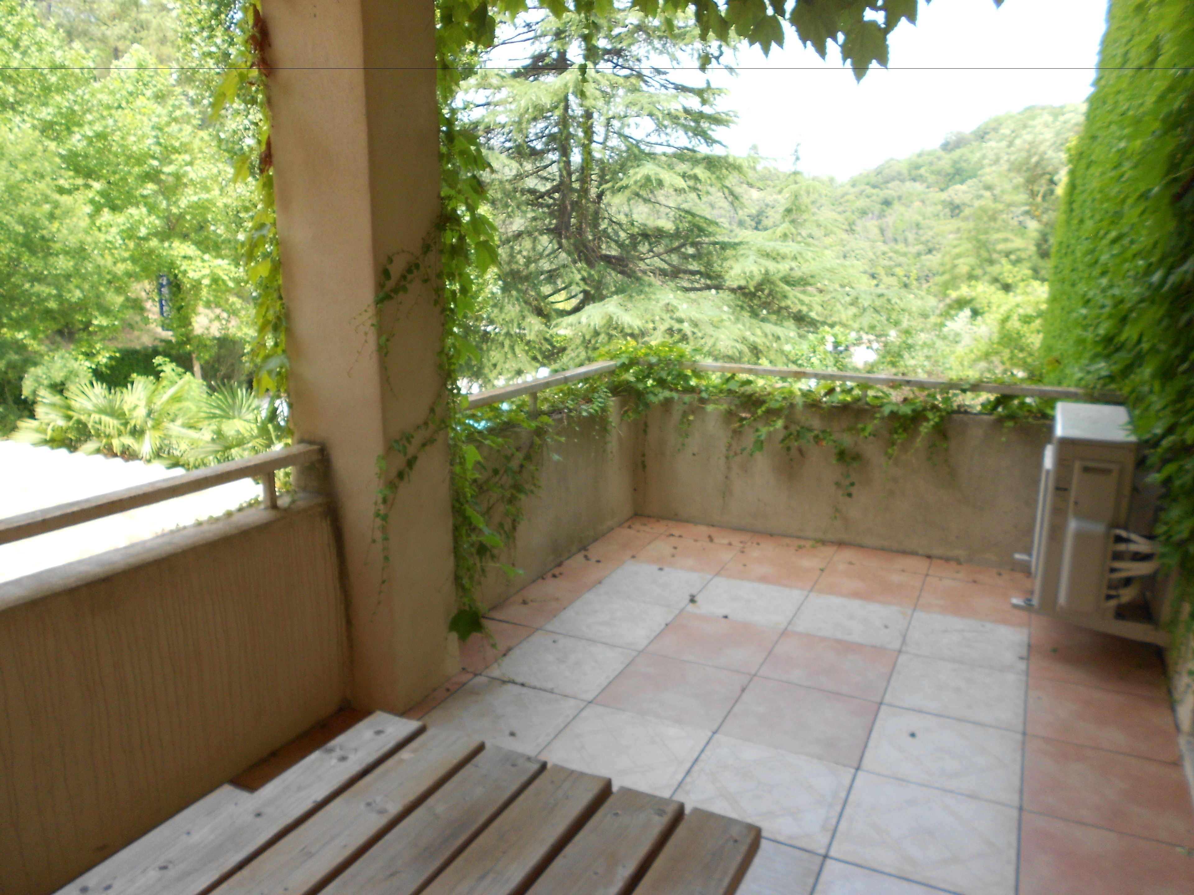 A balcony with a tiled floor, a wooden bench, and a view of lush greenery.