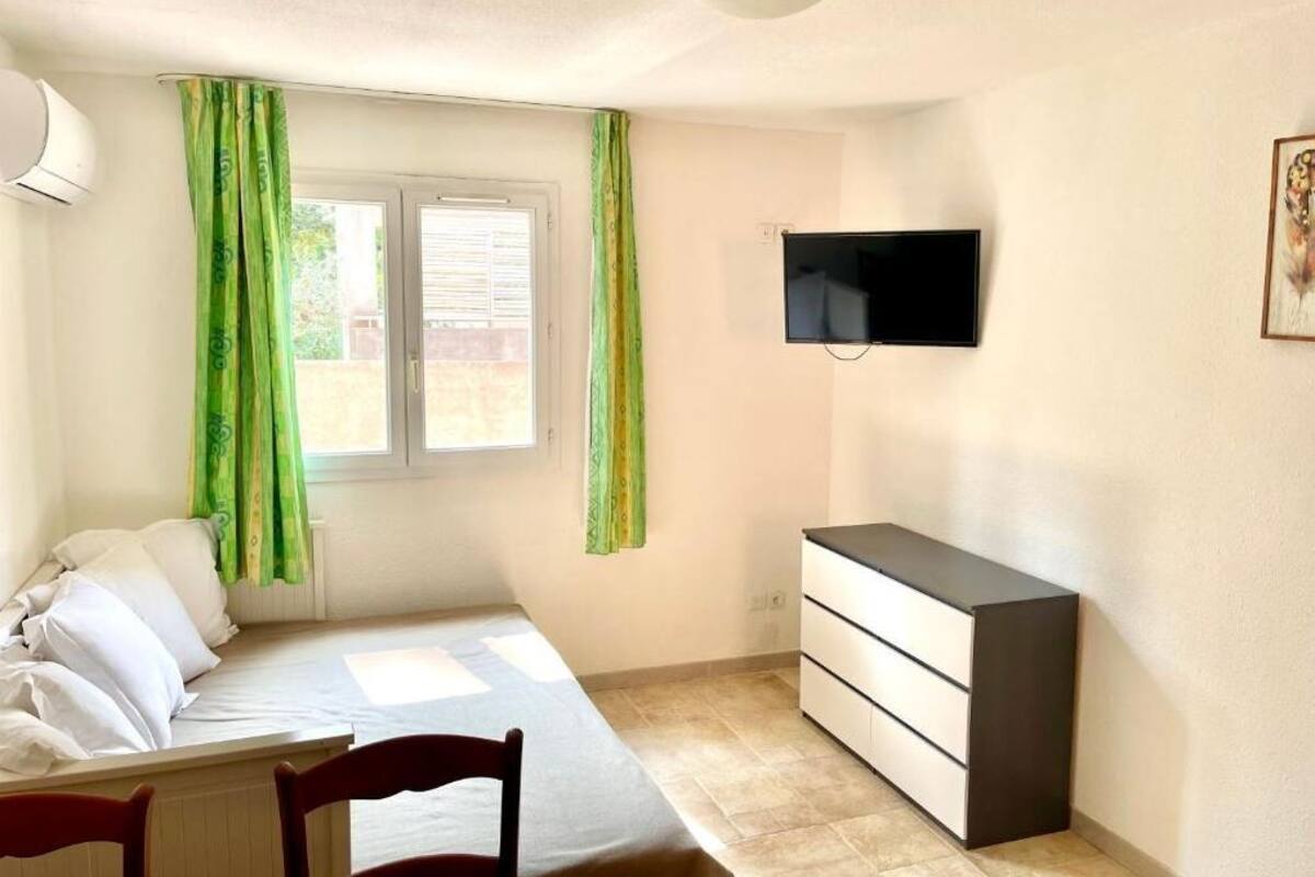 A bedroom with a bed, a dresser, a TV, and green curtains.
