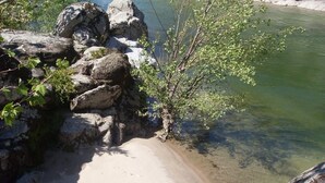 Una costa rocosa con aguas transparentes, una playa arenosa y algo de vegetación.