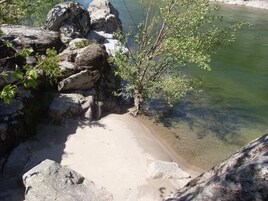 Una costa rocosa con aguas transparentes, una playa arenosa y algo de vegetación.