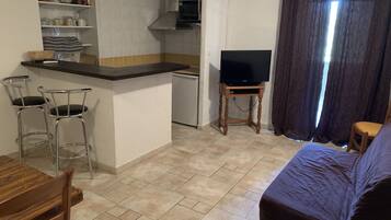 A compact living space with a kitchenette, a dining area with bar stools, a television on a wooden stand, and a bed.